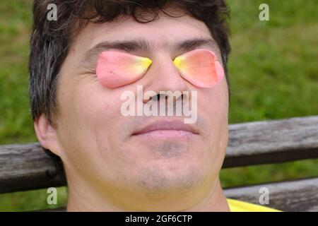The use of rose oil and rose water, rose petals on the eyelids of a man. Rose essential oil. Selective focus Stock Photo