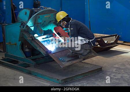 A welder is using an electric arc welding machine in a fabrication workshop. Stock Photo