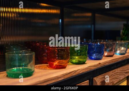 Elegant multi-colored drinking glasses stand in a row on the shelves. Decorative glass jars. Selective focus. Stock Photo