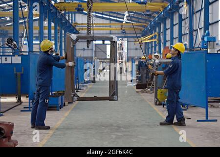 Two workers use hand operated crane to lift a metal frame. Stock Photo