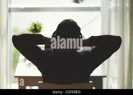 Programmer listening to music in headphones and leaning back in his chair and finishing commenting programming code Stock Photo