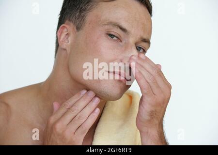 Handsome attractive young man touching his face looking for imperfections, wrinkles and pimples Stock Photo
