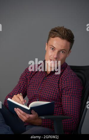 Attractive fit young businessman taking notes and writing down ideas in planner Stock Photo