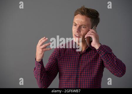 Frowning emotional young man talking on phone with coworker Stock Photo