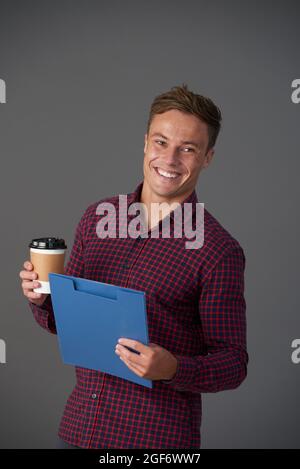 Positive young entrepreneur holding clipboard with document holding cup of take out coffee Stock Photo