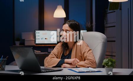 Businesswoman with headphones discussing marketing statistics planning business strategy. Entrepreneur woman talking with her collegues during online videocall conference company meeting in evening Stock Photo