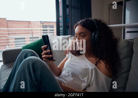 Mixed race female teenage texting on cellular device relaxing on couch Stock Photo