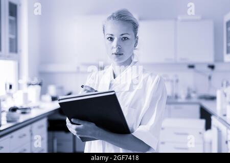 Portrait of young, confident female health care professional taking notes during inventory in scientific laboratory or medical doctors office Stock Photo