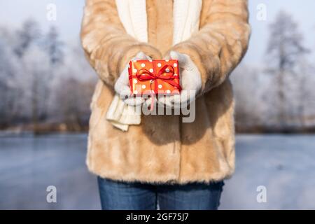 Woman holding christmas present in snowy landscape. Small red gift box in female hands Stock Photo