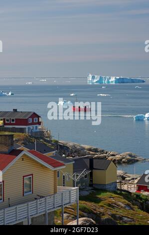 Wooden houses in front of a bay with fishing boat and icebergs, Arctic, Disko Bay, Ilulissat, Greenland, Denmark Stock Photo