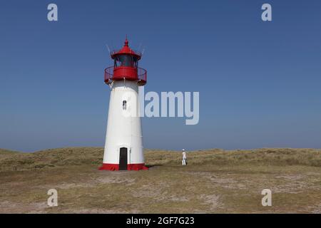 Red and white lighthouse List-West, in front of it single tourist, dressed in white, elbow, Sylt, East Frisian Islands, Schleswig-Holstein, Germany Stock Photo