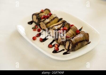 Fried stuffed eggplant with cheese and meat, tomatoes and sauce on white plate, selective focus Stock Photo