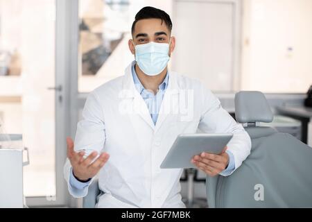 Portrait of handsome arab dentist in medical mask using digital tablet Stock Photo