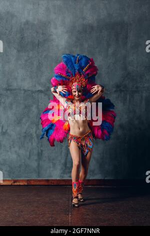 Woman in brazilian samba carnival costume with colorful feathers plumage  with mobile phone take selfie in old entrance with big window. Stock Photo