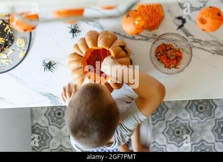 Halloween pumpkin cutting process, process of making Jack-o-lantern. Boy hands with knife, leftovers of pumpkin on the kitchen table.  Stock Photo