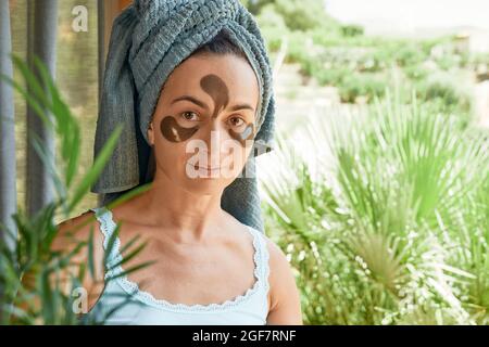 Morning skincare routine. Middle age woman with wrinkles and hydrogel under-eye patches, looking at camera on nature background. Lifting anti-wrinkle Stock Photo