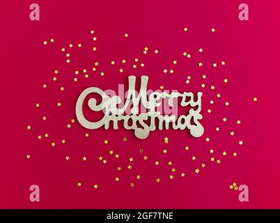 Merry Christmas gold greeting message and golden stars confetti on red background. Top view. Bright Christmas greeting card. Stock Photo