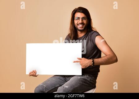 Handsome middle-eastern young man got vaccinated, holding blank board Stock Photo
