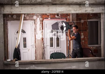 Behind the scene. Filmmaking lighting technician electric engineer adjusting reflector and setup lights diffusion intensity for movie film scene. Ligh Stock Photo