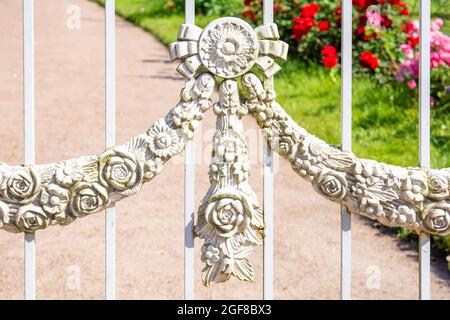Decorative element of vintage forged white fence with garlands of flowers. Details, structure and ornaments of forged iron gate. Floral decorative orn Stock Photo