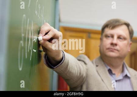 Professor of the Department of Applied Mathematics in classroom at the blackboard writes formulas for students. Stock Photo