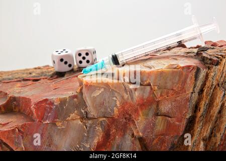 Injection needle placed on rock with pair of dice reflects concept of vaccinations needed to avoid rocky danger and to not play games with personal or