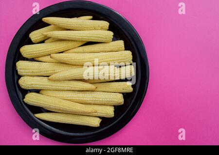 Fresh and organic Babycorn vegetble whole pieces arranged on black plate on pink solid background blank space to write text wallpaper poster Stock Photo