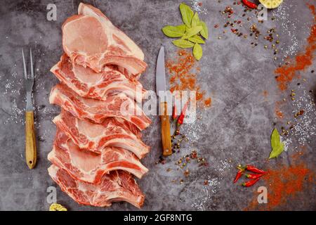 Raw pork chops bone in with spices on dark background. Stock Photo