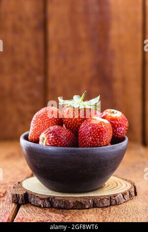 fresh strawberries in handmade clay bowl with wooden background and copy space Stock Photo