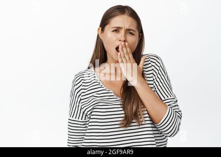 Young woman yawning, looking bored and unamused at camera, white background Stock Photo