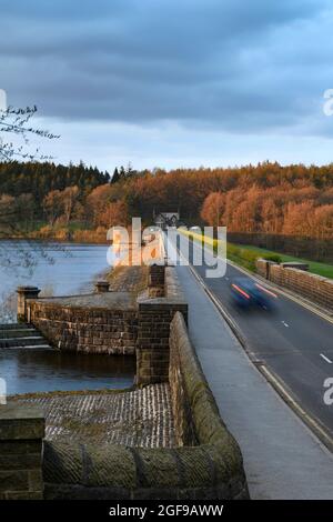 Embankment wall, car lights on road, forest trees, autumn colours, grey evening clouds - Fewston Reservoir, Washburn Valley, Yorkshire, England, UK. Stock Photo