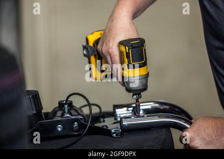 An auto repair man using a drill and fixing a car part in an auto repair shop Stock Photo