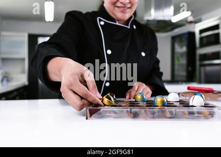 hand of latin woman pastry chef wearing black uniform in process of preparing delicious sweets chocolates at kitchen in Mexico Latin America Stock Photo