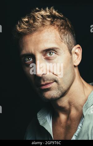 Portrait of charming man with blond hair and green and brown eyes. Black background. Green shirt. Stock Photo