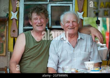 An adult son and an old man father have fun laughing, hugging and looking at the camera. Stock Photo