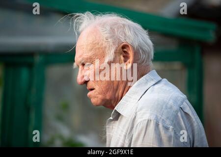 An old gray-haired man with a concerned face and wrinkles in profile. Stock Photo