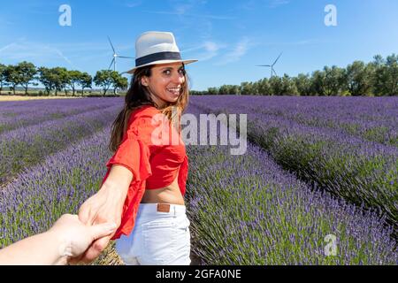 Young woman walking in a lavender field and turning back while holding somebody’s hand. Concept of well-being and love for nature.