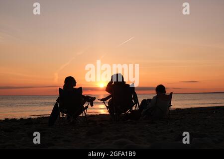 Gower, Swansea, UK. 24th August 2021.  UK weather:  Enjoying the view, people gather to watch setting sun on a dry, fine  and sunny evening at Llangennith beach on the Gower peninsula. The outlook for the next few days is for similarly fine weather with some warm spells.Credit: Gareth Llewelyn/Alamy Live News Stock Photo