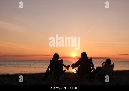 Gower, Swansea, UK. 24th August 2021.  UK weather:  Enjoying the view, people gather to watch setting sun on a dry, fine  and sunny evening at Llangennith beach on the Gower peninsula. The outlook for the next few days is for similarly fine weather with some warm spells.Credit: Gareth Llewelyn/Alamy Live News Stock Photo