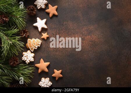 Christmas homemade assorted glazed cookies and frame of fir tree and cones on brown background. New Year holiday treats. Top view. Xmas greeting card. Stock Photo