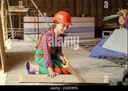 girl working with wood in workshop. carpentry and woodwork concept. Portrait of a cute kid posing as a carpenter, with a handsaw. working as Stock Photo