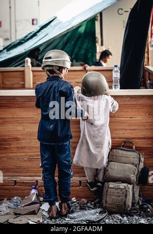 Kabul, Afghanistan. 24th Aug, 2021. Afghan children play with military helmets while awaiting for evacuation at Hamid Karzai International Airport during Operation Allies Refuge August 24, 2021 in Kabul, Afghanistan. Credit: Planetpix/Alamy Live News