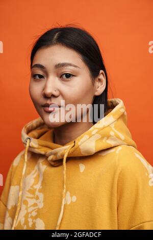 Asian teen girl wearing hoodie posing and looking at camera isolated over orange background Stock Photo