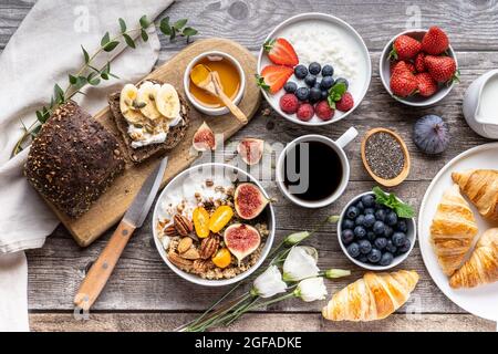 A table for a healthy breakfast with rye whole-grain bread, butter, granola, fresh berries, honey, porridge and croissants . Top view. Stock Photo