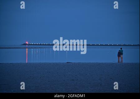 Beautiful evening view couple standing in water and waiting for blue sturgeon Moon rising over Irish sky Dun Laoghaire harbor on August 23, 2021 Stock Photo
