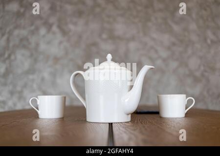 white tea set teapot and two cups stand on a brown table Stock Photo