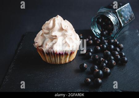 Appetizing baked vanilla muffin with currants on a black serving board. Delicious chocolate cupcake on a dark background with currants scattered from Stock Photo