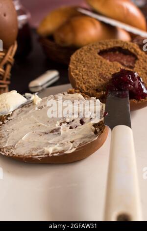 Round brown bread with white butter and  blackberry jam on a white plate with some breads in a bascket at background Stock Photo