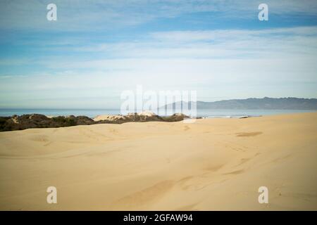 Sand dunes leading to Pacific Ocean on cloudy winter's day, with hazy gray mountains on the horizon Stock Photo