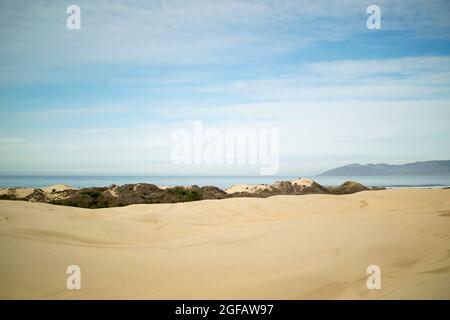 Sand dunes leading to Pacific Ocean on cloudy winter's day, with hazy gray mountains on the horizon Stock Photo